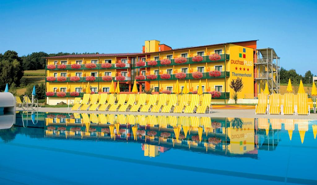 ein Hotel mit gelben Stühlen und einer Reflexion im Wasser in der Unterkunft Thermenhotel PuchasPLUS Stegersbach in Stegersbach
