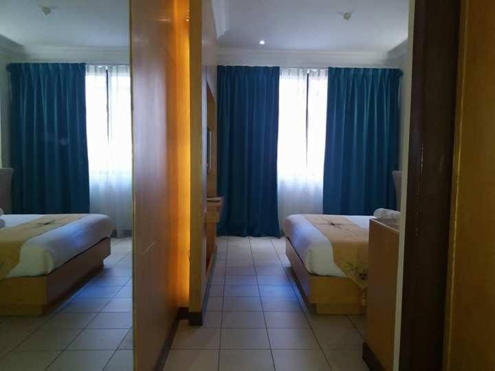 Habitación de hotel con 2 camas y cortinas azules en Fratini's Hotel Labuan en Labuan