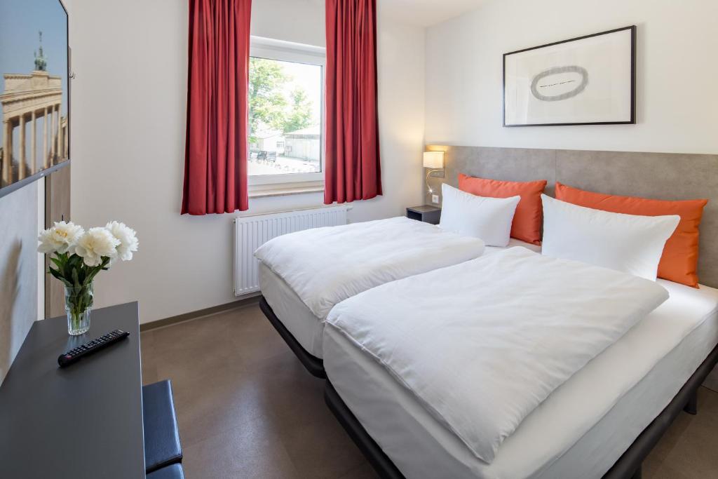 a bedroom with two beds and a table with a vase of flowers at TRIO Apartment Hotel Berlin in Berlin