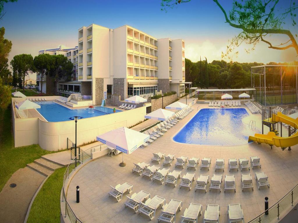 a resort with a pool and chairs and a building at Hotel Adria in Biograd na Moru