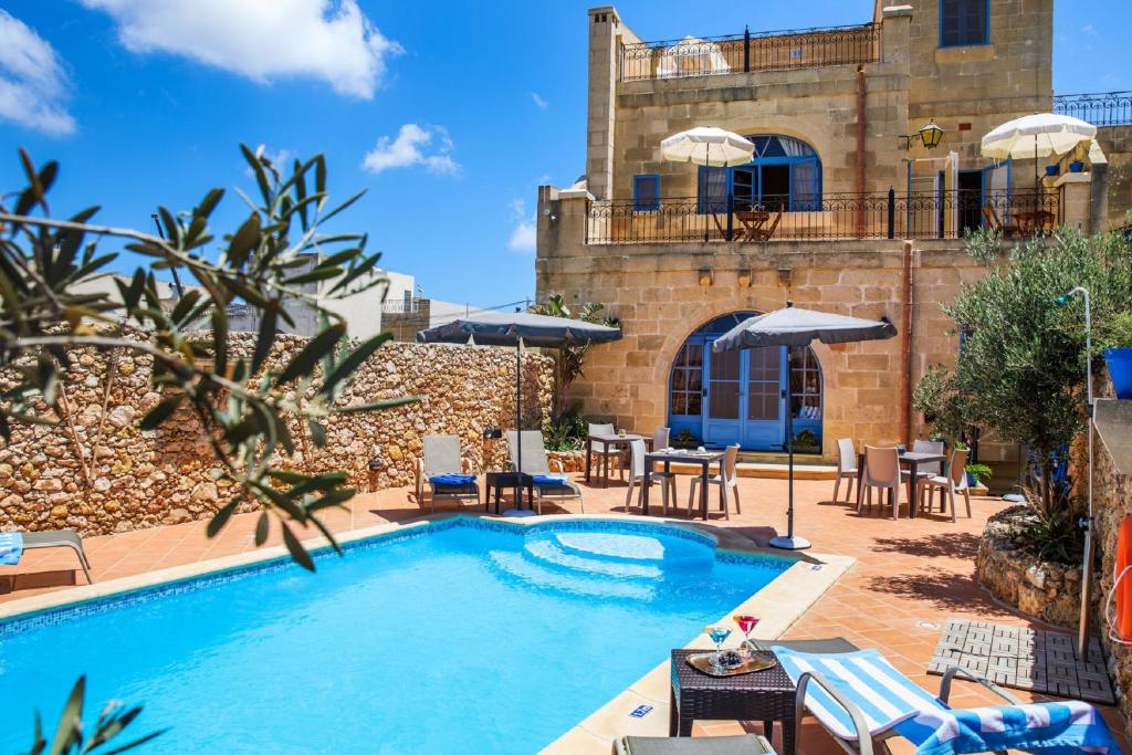 einem Pool vor einem Gebäude mit Tischen und Stühlen in der Unterkunft L'Ghorfa in Xagħra