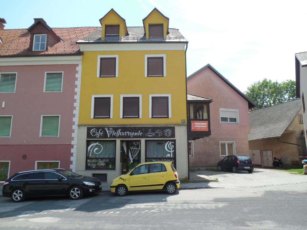 Cafe Vielharmonie Apart-Pension في Maria Lankowitz: مبنى أصفر مع سيارة متوقفة في موقف للسيارات