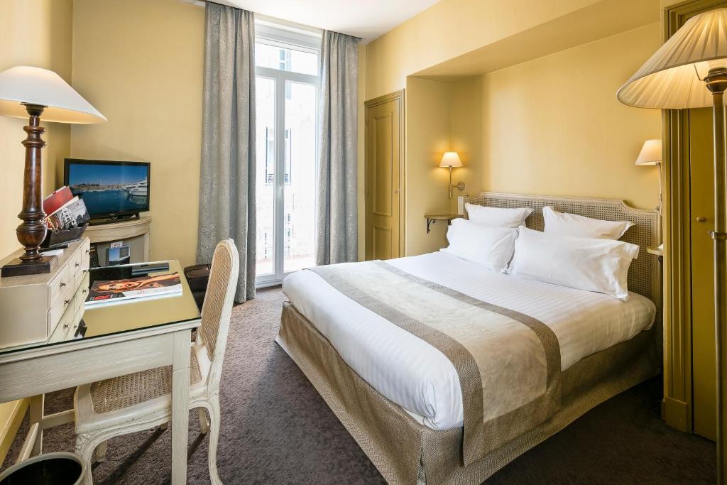 a hotel room with a bed and a desk and a window at Le Cavendish in Cannes