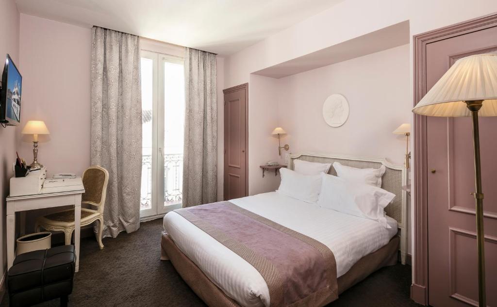 a hotel room with a bed and a desk and a window at Le Cavendish in Cannes