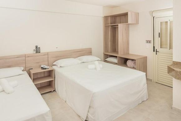 a white bedroom with a large white bed and shelves at Hotel Dois H in Joinville