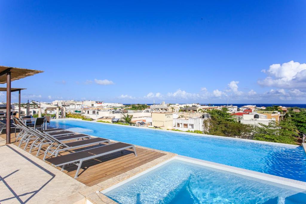 a large swimming pool with lounge chairs and the ocean at Papaya 15 Apartments in Playa del Carmen