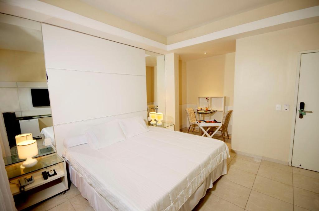 a bedroom with a large white bed and a table at Hotel Jangadeiro in Recife