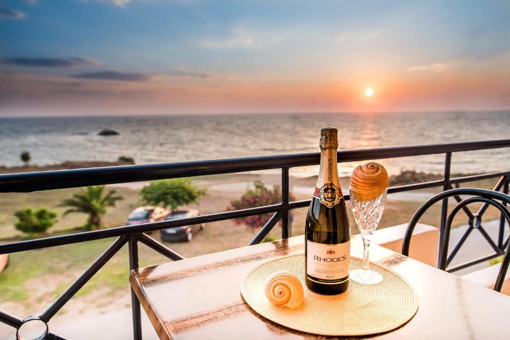 ミティカスにあるFaros Apartmentsのビーチのテーブルに置いたグラス1杯とワイン1本