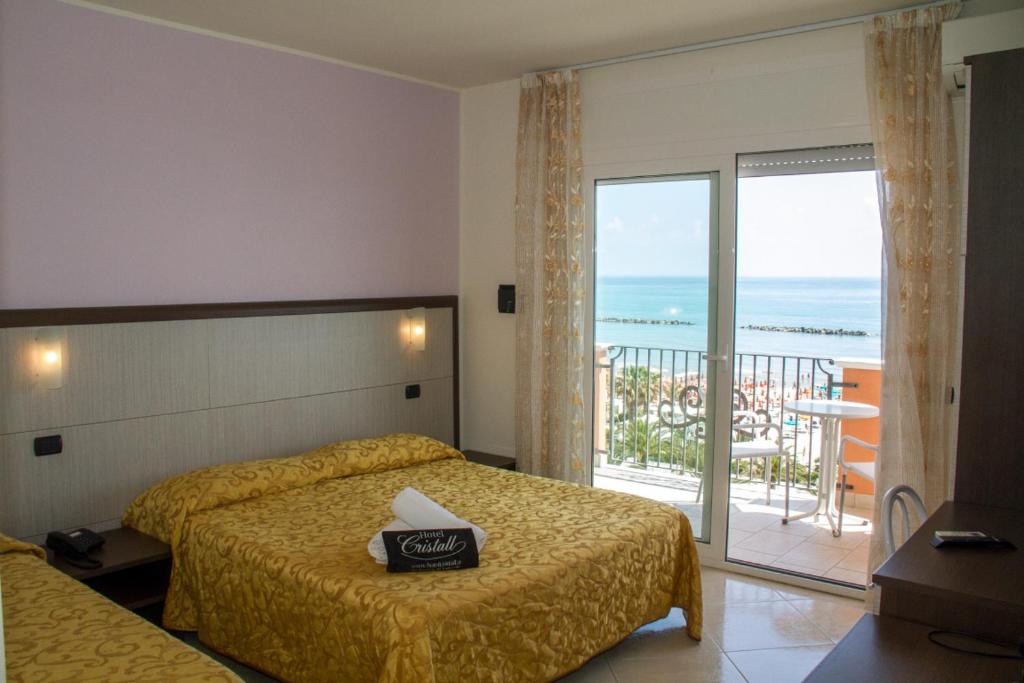 サン・ベネデット・デル・トロントにあるHotel Cristallのベッド1台、海を望むバルコニーが備わるホテルルームです。