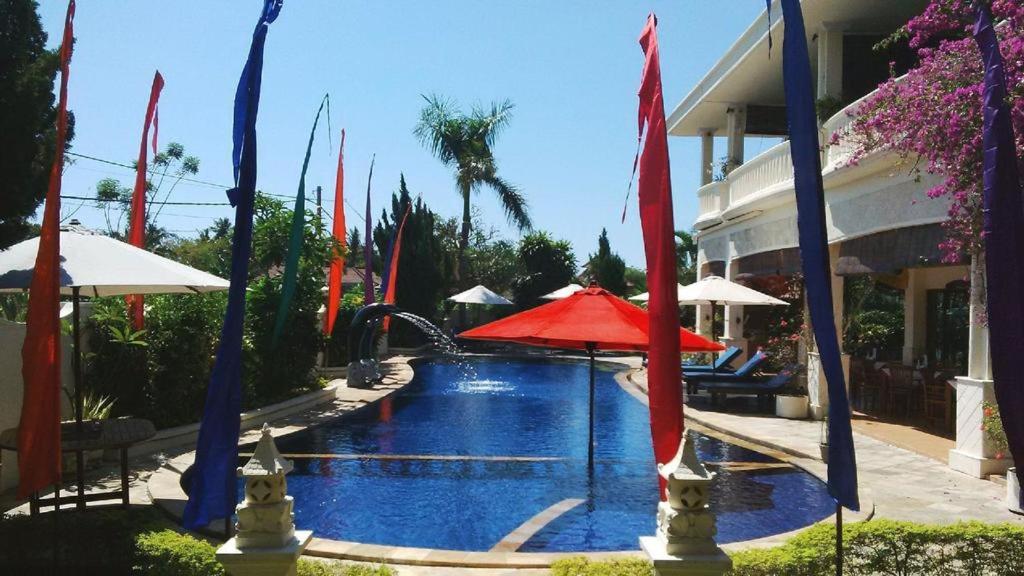 a swimming pool with a red umbrella and a fountain at Bali Paradise Hotel Boutique Resort in Lovina