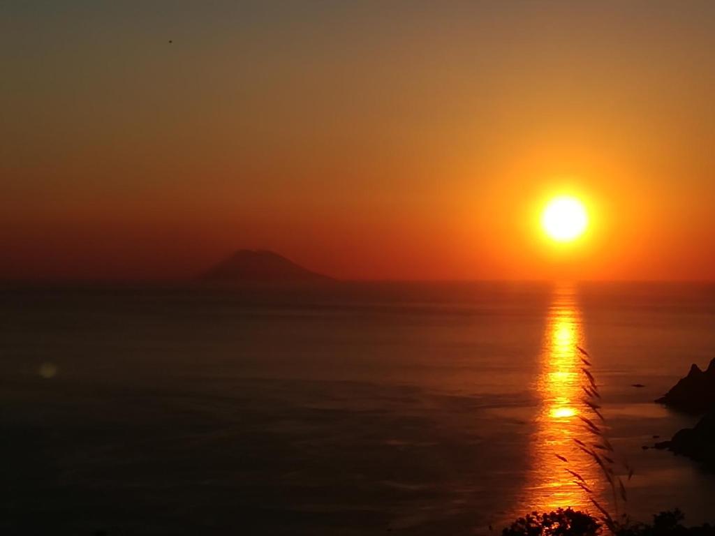 um pôr-do-sol sobre o oceano com o sol no céu em L'Agave em Ricadi