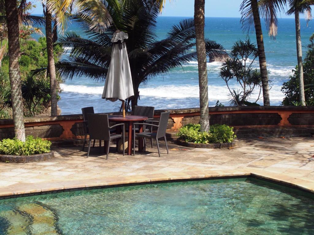 une terrasse avec une table et un parasol et l'océan dans l'établissement Gajah Mina Beach Resort, à Selemadeg