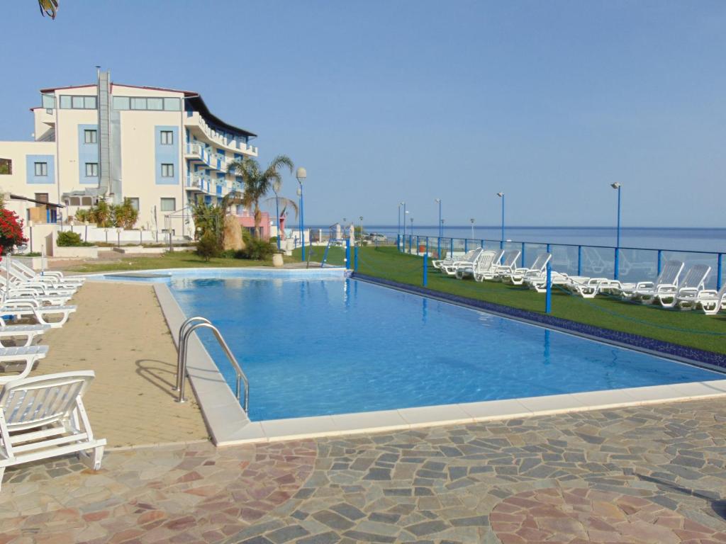 a large swimming pool with white chairs and the ocean at Tus'Hotel in Castel di Tusa