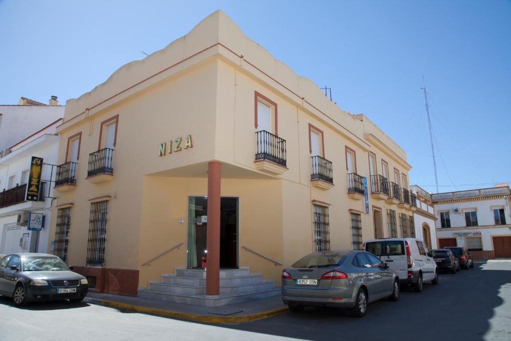 un edificio amarillo con coches estacionados frente a él en Hostal Niza, en San Juan del Puerto