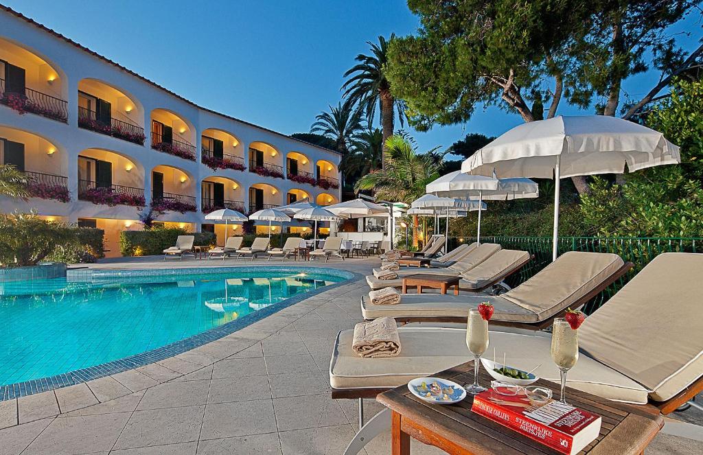 a hotel room with a pool, chairs, tables and umbrellas at Hotel Della Piccola Marina in Capri
