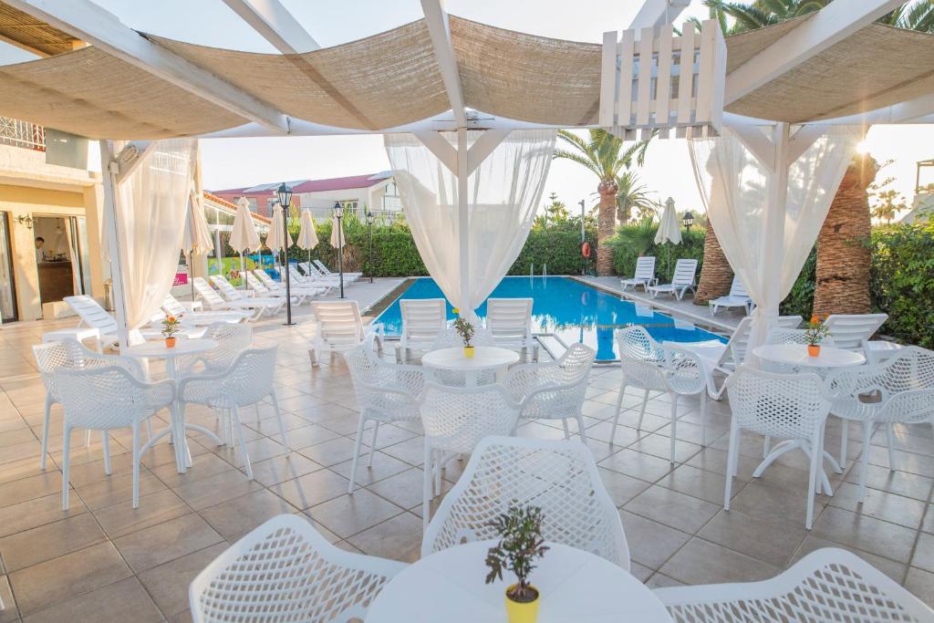 a patio with white tables and chairs and a pool at Creta Aquamarine Hotel in Platanes