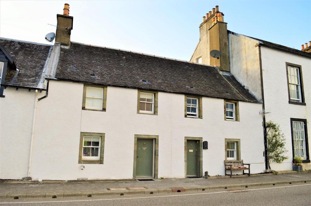 a white house with green doors on a street at Newton Cottage North in Inveraray