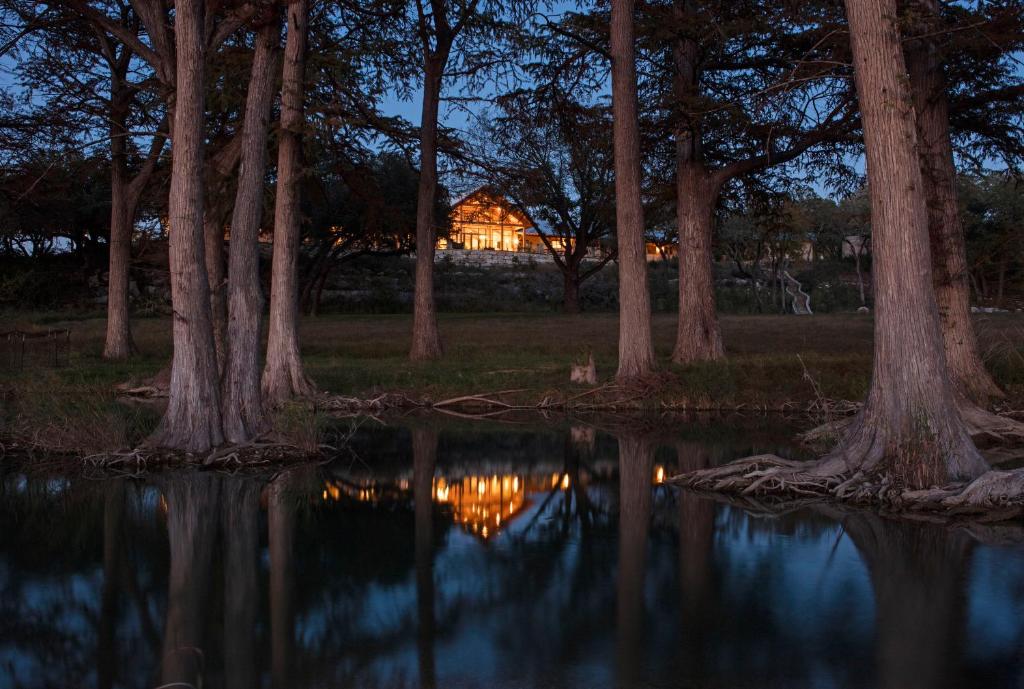 una casa en el bosque con un reflejo en el agua en Joshua Creek Ranch, en Boerne