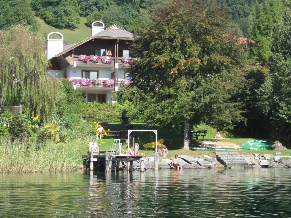a house on the shore of a lake with people on a dock at Ferienwohnung Moser am See in Millstatt