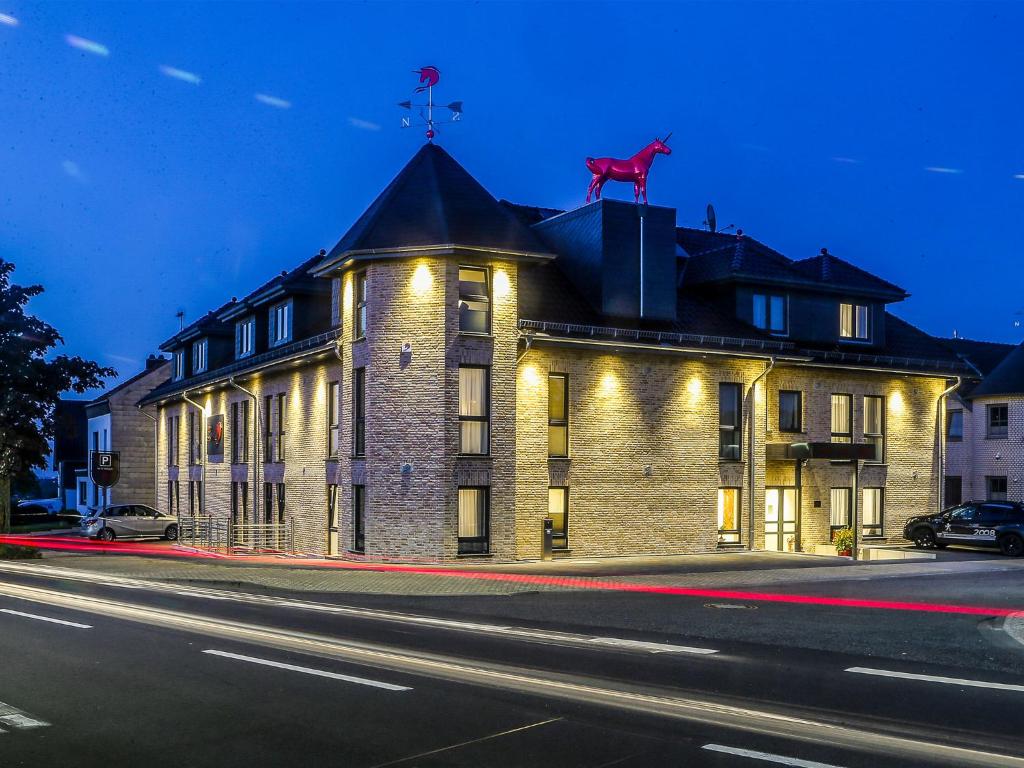 ein großes Backsteingebäude mit einem roten Pferd auf dem Dach in der Unterkunft Hotel Rotes Einhorn **** in Düren - Eifel