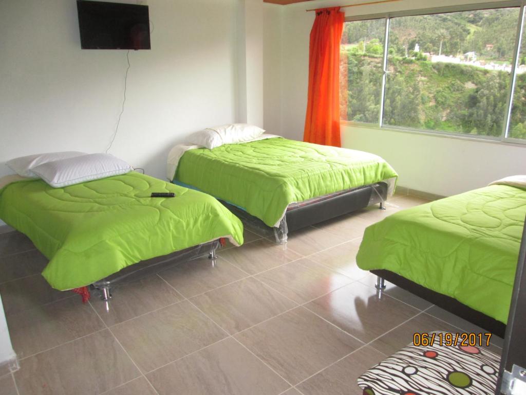 a room with two beds with green blankets and a window at Los Recuerdos de Florito y Leo in Monguí