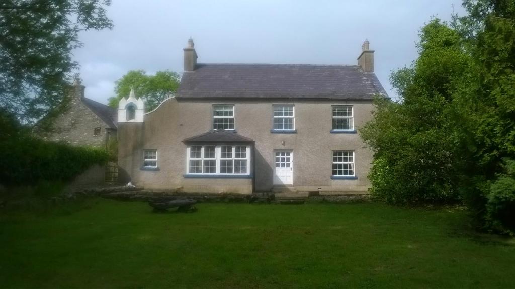 una casa vieja con un patio de hierba delante de ella en Creevy Lodge en Castlederg