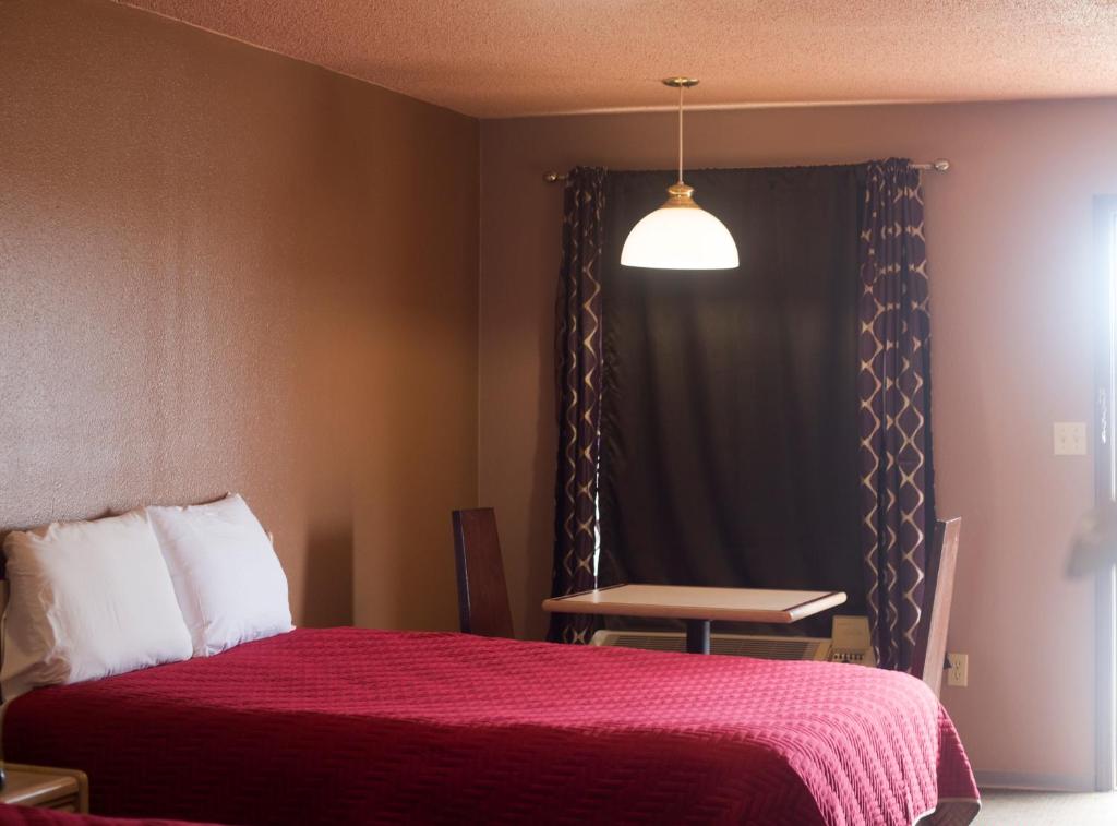 a bedroom with a bed with a red blanket and a table at Hickory House Inn in Dexter