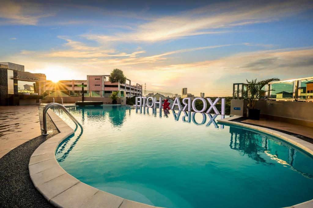 a large swimming pool in a city with the sun setting at Ixora Hotel Penang in Perai