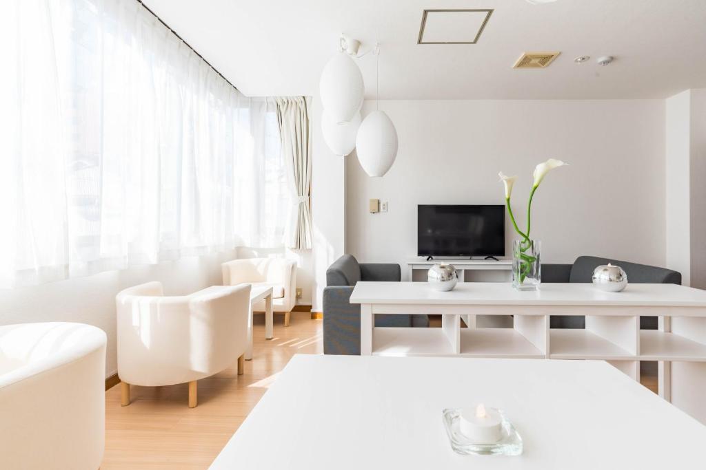 Bijou Suites Ferries Wheel View في أوساكا: غرفة معيشة بيضاء مع أثاث أبيض وتلفزيون