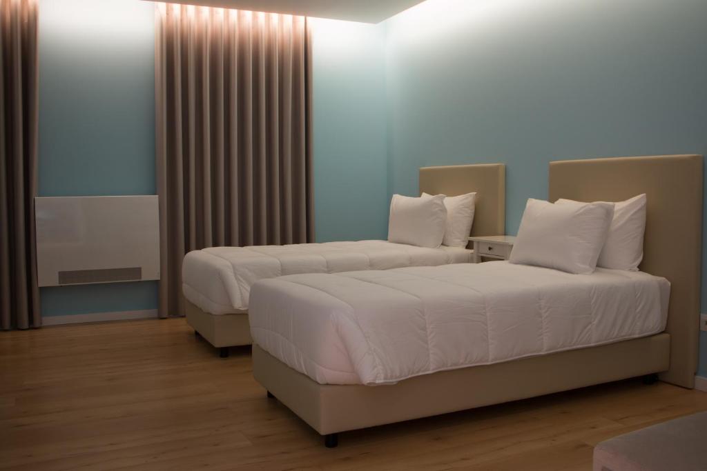 two beds in a hotel room with white pillows at Feira Hostel & Suites in Santa Maria Da Feira