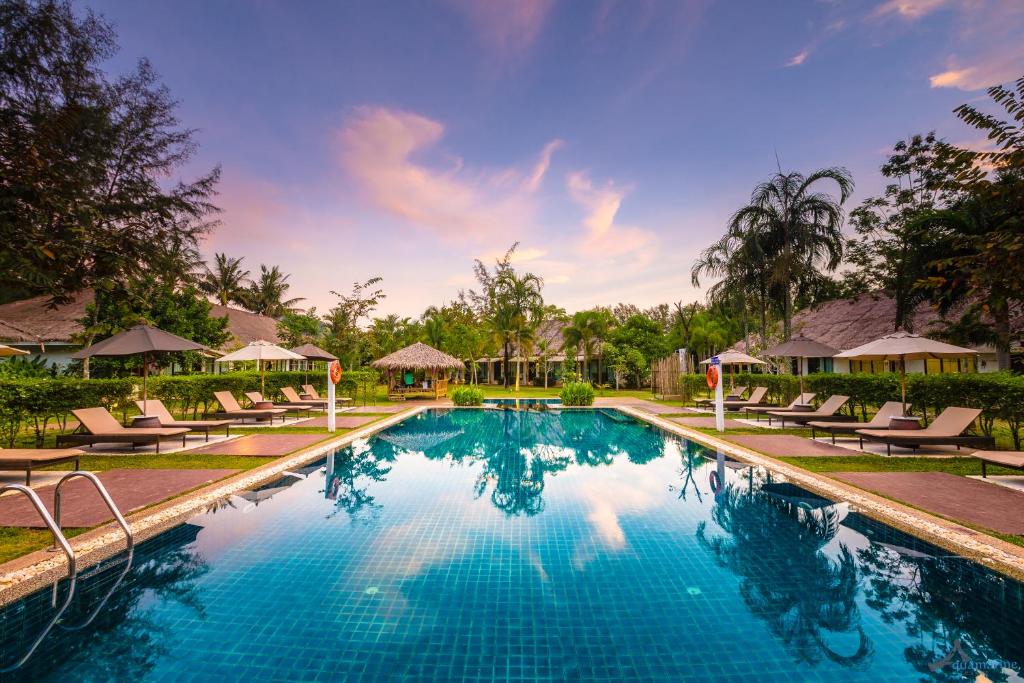 a pool at a resort with chairs and trees at Krabi Aquamarine Resort - SHA Plus in Ao Nang Beach