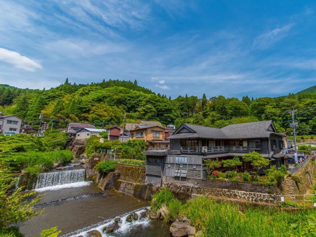 a house next to a river with a waterfall at Takaosou in Yufuin