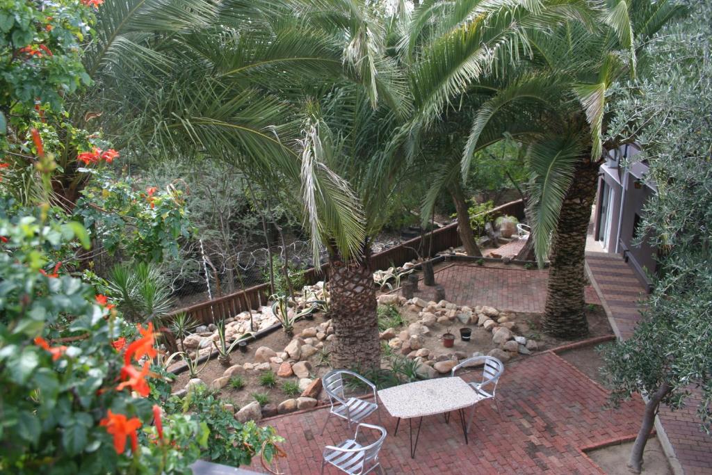 a garden with a bench and palm trees and flowers at De Vagebond Hotel-Pension in Windhoek