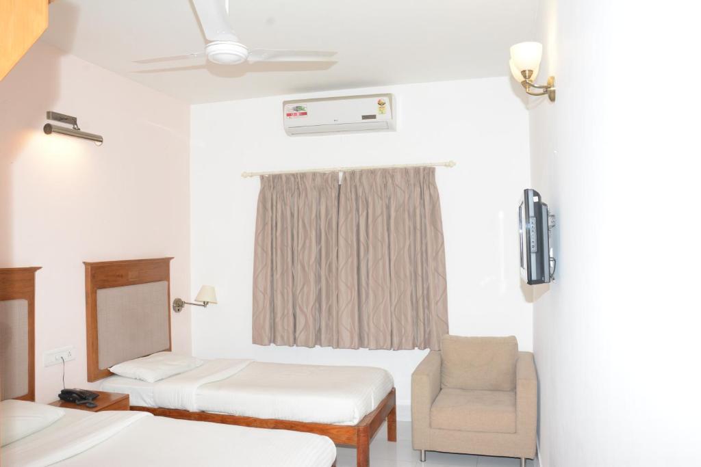 a hotel room with two beds and a chair at Sai Towers in Puttaparthi