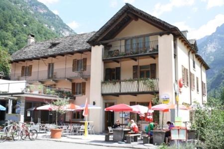 ein Gebäude mit Tischen und Sonnenschirmen davor in der Unterkunft Ristorante Alpino in Sonogno