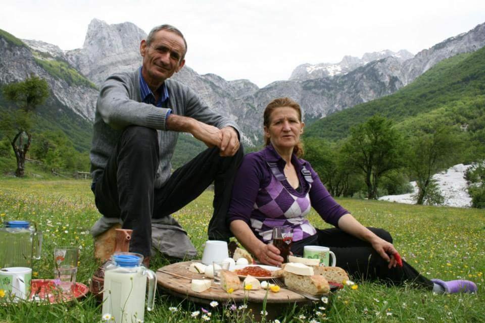 Ein Mann und eine Frau sitzen auf einem Feld mit einem Picknick. in der Unterkunft Kulla e Sadri Lukes in Theth