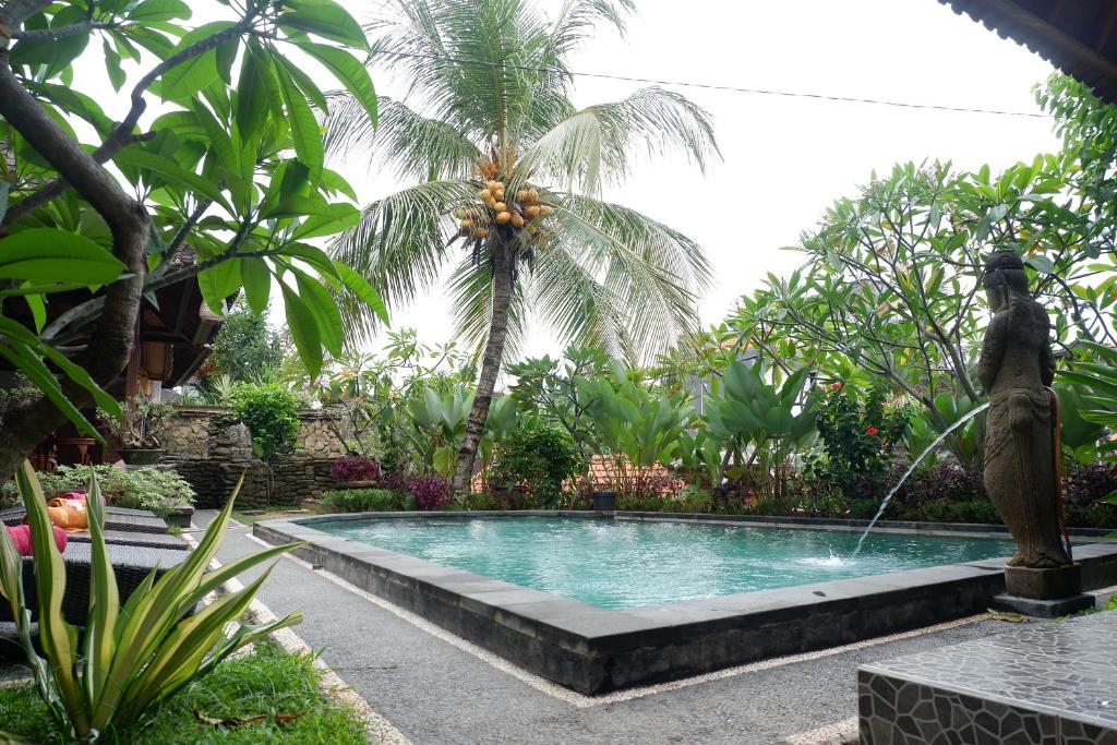 a swimming pool in a garden with a fountain at Budi House Bungalows in Ubud