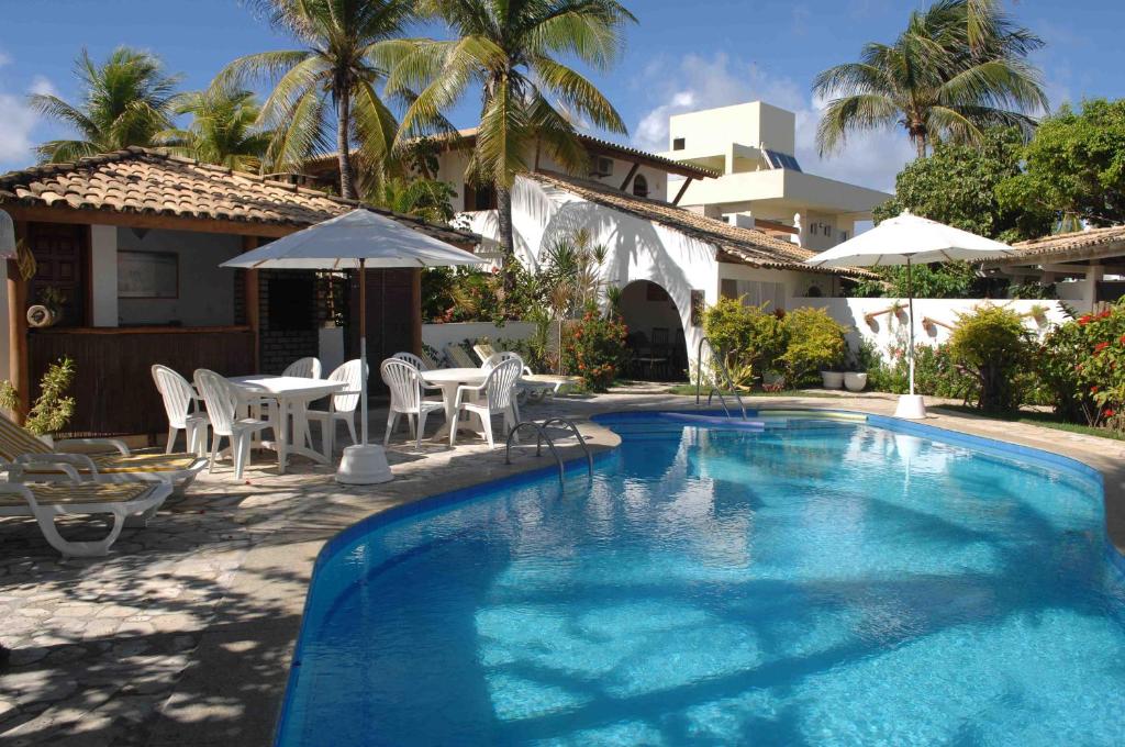 a swimming pool with chairs and umbrellas next to a house at Casa das Ondas Guarajuba in Guarajuba