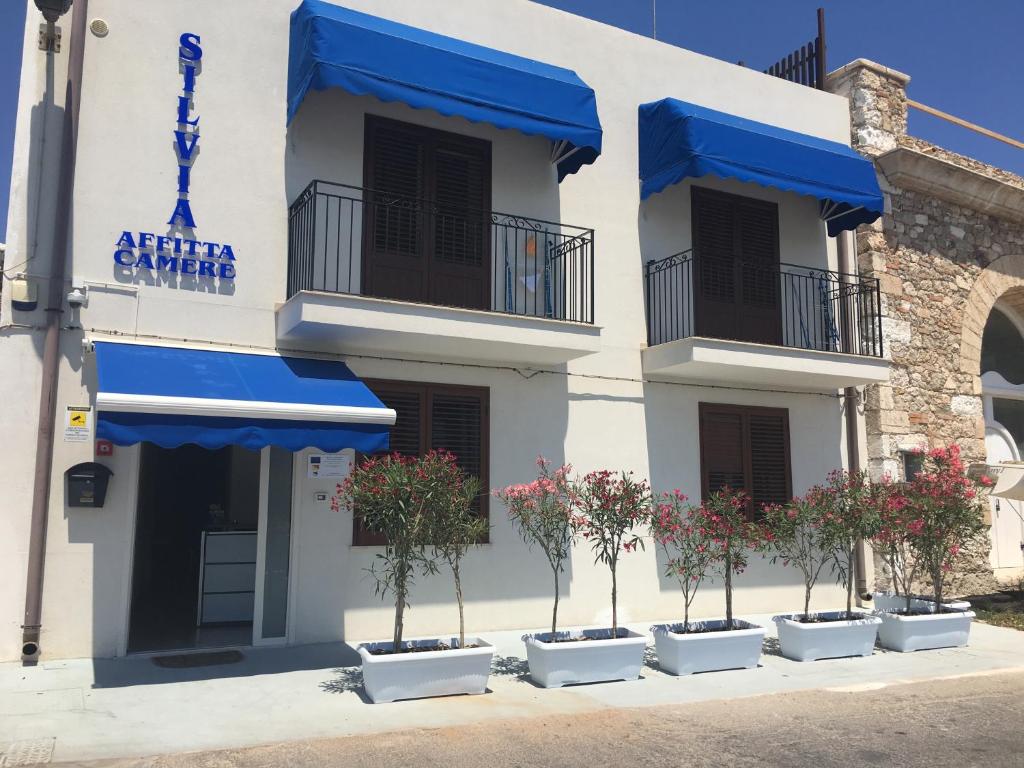 a building with blue awnings and potted trees in front at Silvia Affittacamere in Lampedusa
