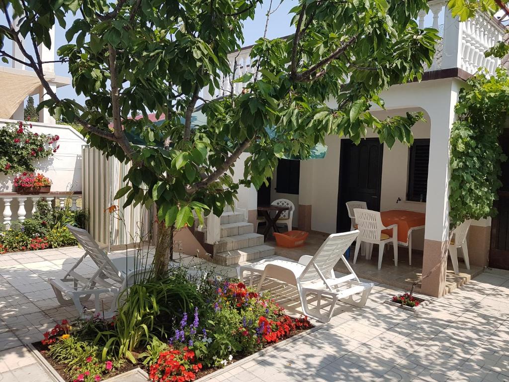 um pátio com cadeiras brancas, uma árvore e flores em Apartment Sena em Privlaka