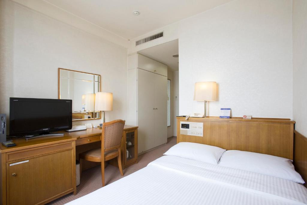 千葉市にあるテトランゼ幕張稲毛海岸ホテルのベッド、デスク、テレビが備わるホテルルームです。