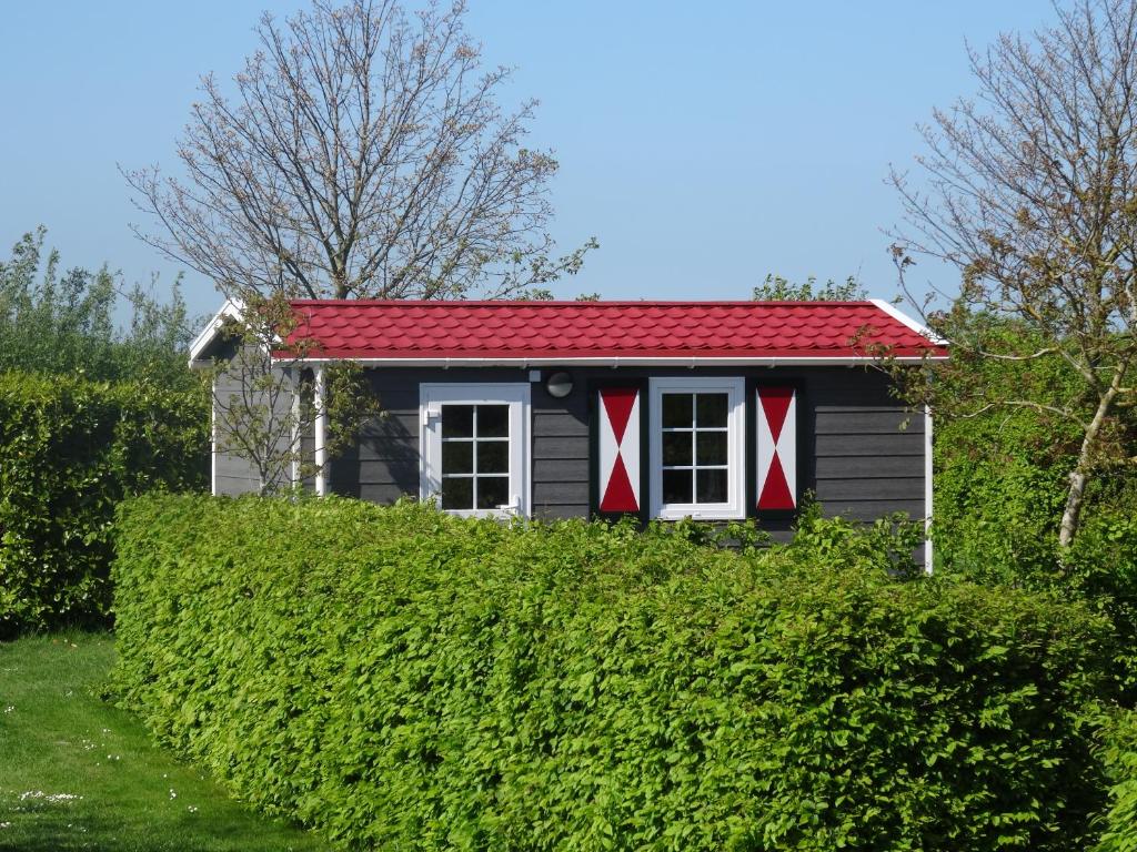 a small house with a red roof over a hedge at zeeuwse chalet voor 2 personen in Serooskerke