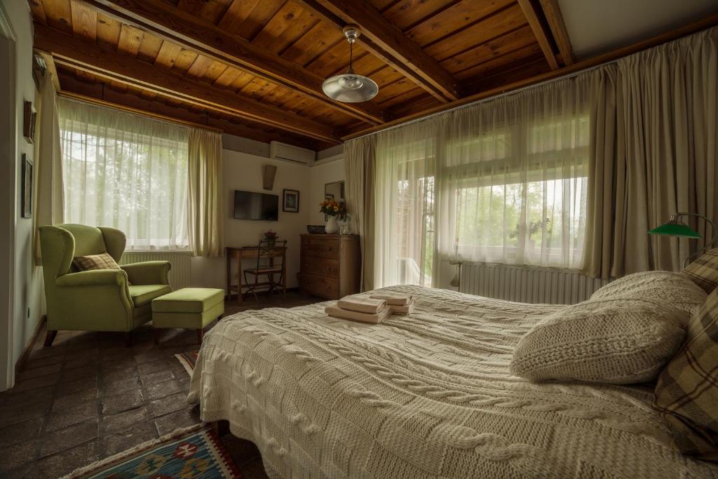 a bedroom with a bed and a chair and windows at Káli Art Inn Panzió in Köveskál
