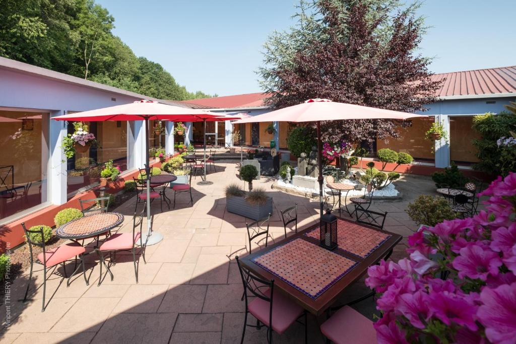 an outdoor patio with tables and chairs and umbrellas at Hôtel Logis Atrium Epinal Golbey Chavelot in Épinal