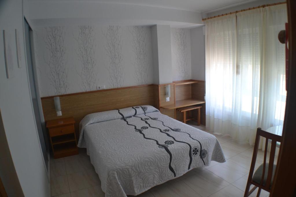 a bedroom with a bed and a desk and a window at Hostal Casa Maria in Portonovo