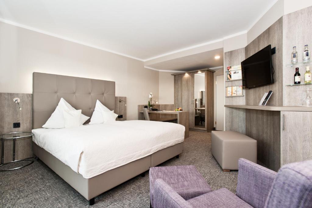 a bedroom with a large white bed and two purple chairs at Ringhotel Am Stadtpark in Lünen