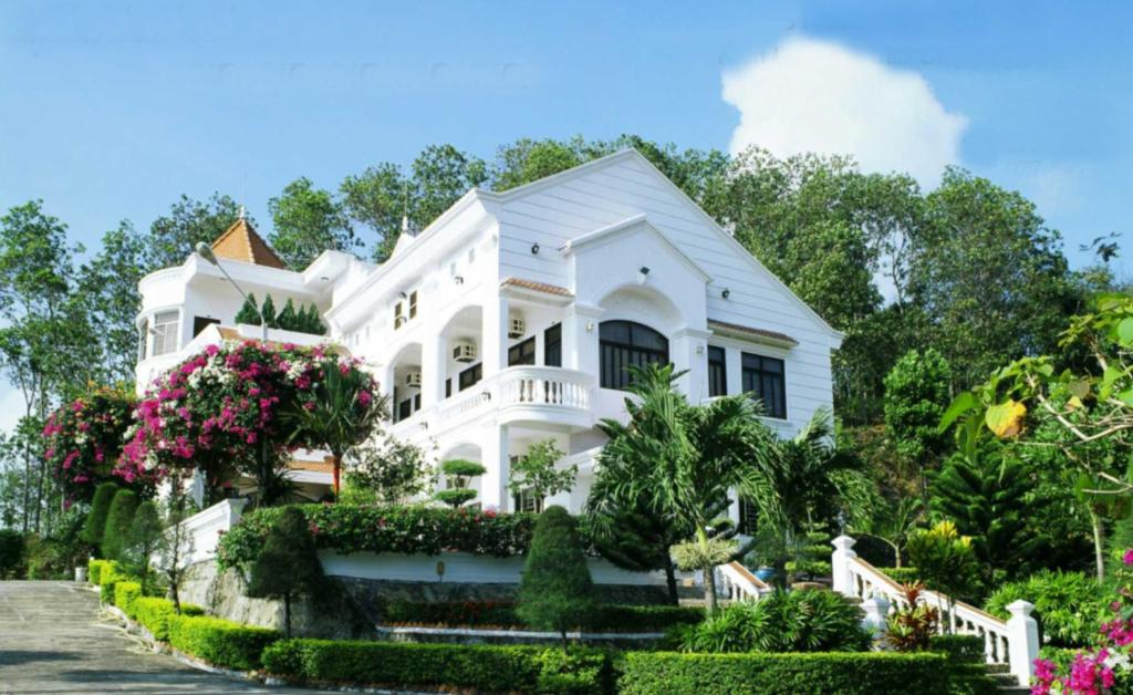 een wit huis met bloemen en bomen bij Green Hill Guest House in Ba Hòn