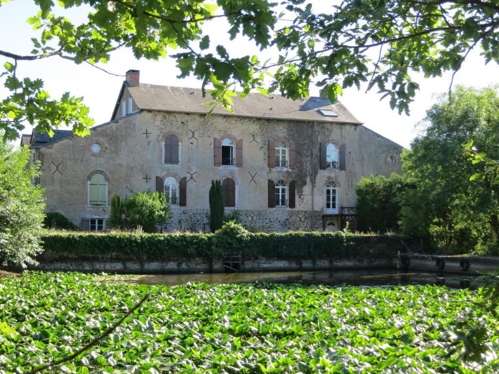 una vieja casa de piedra con un seto delante de ella en Chambres d'hôtes du Moulin de la Chaussee, en Saint-Denis-dʼOrques