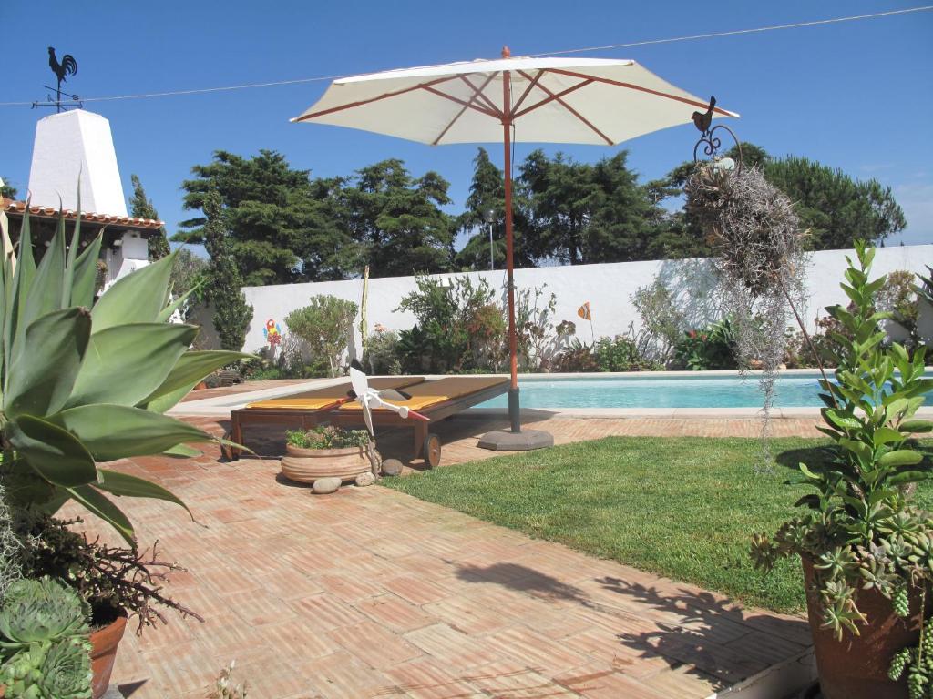 a patio with an umbrella and a swimming pool at Casa dos Cactos in Vila Nova de Milfontes