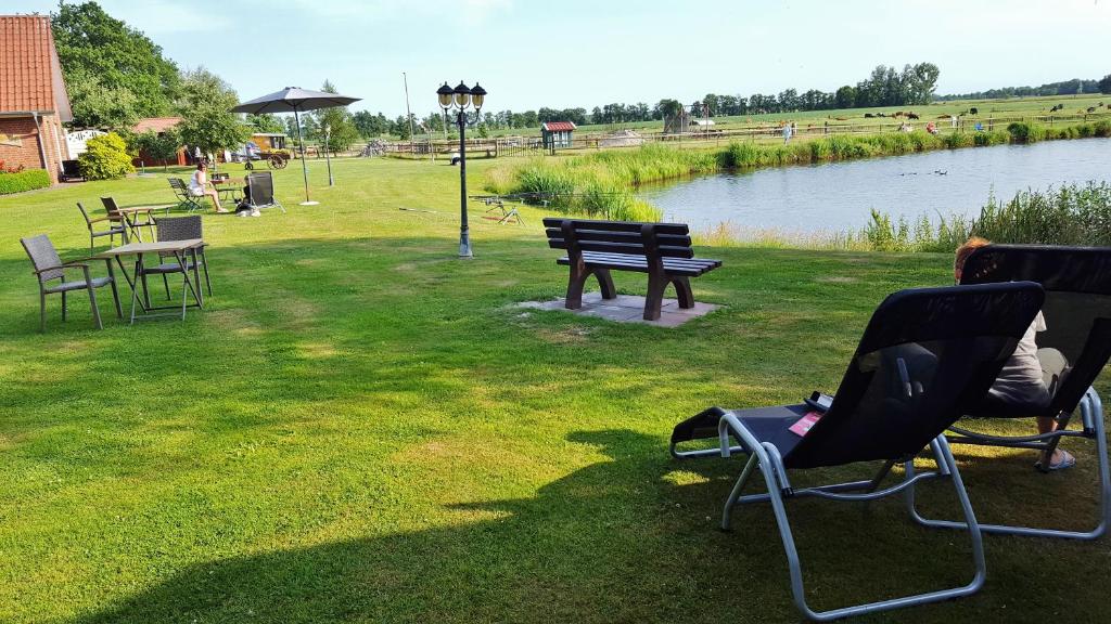 ein Park mit Stühlen und Tischen und eine Bank neben einem See in der Unterkunft Pension am Birkensee in Detern